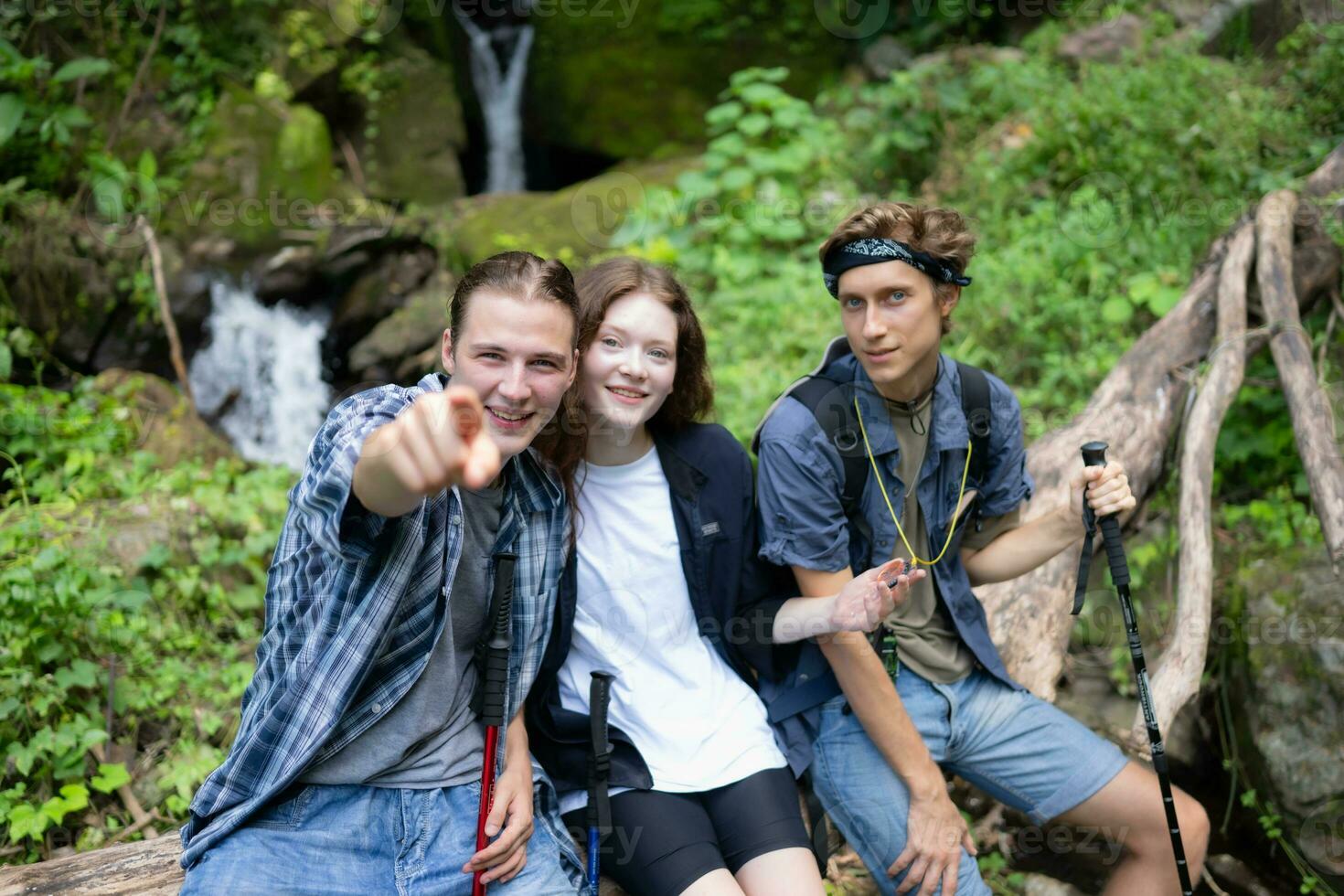 grupo de amigos con mochilas y palos sentado en un caído árbol, tomar un descanso durante el caminata foto