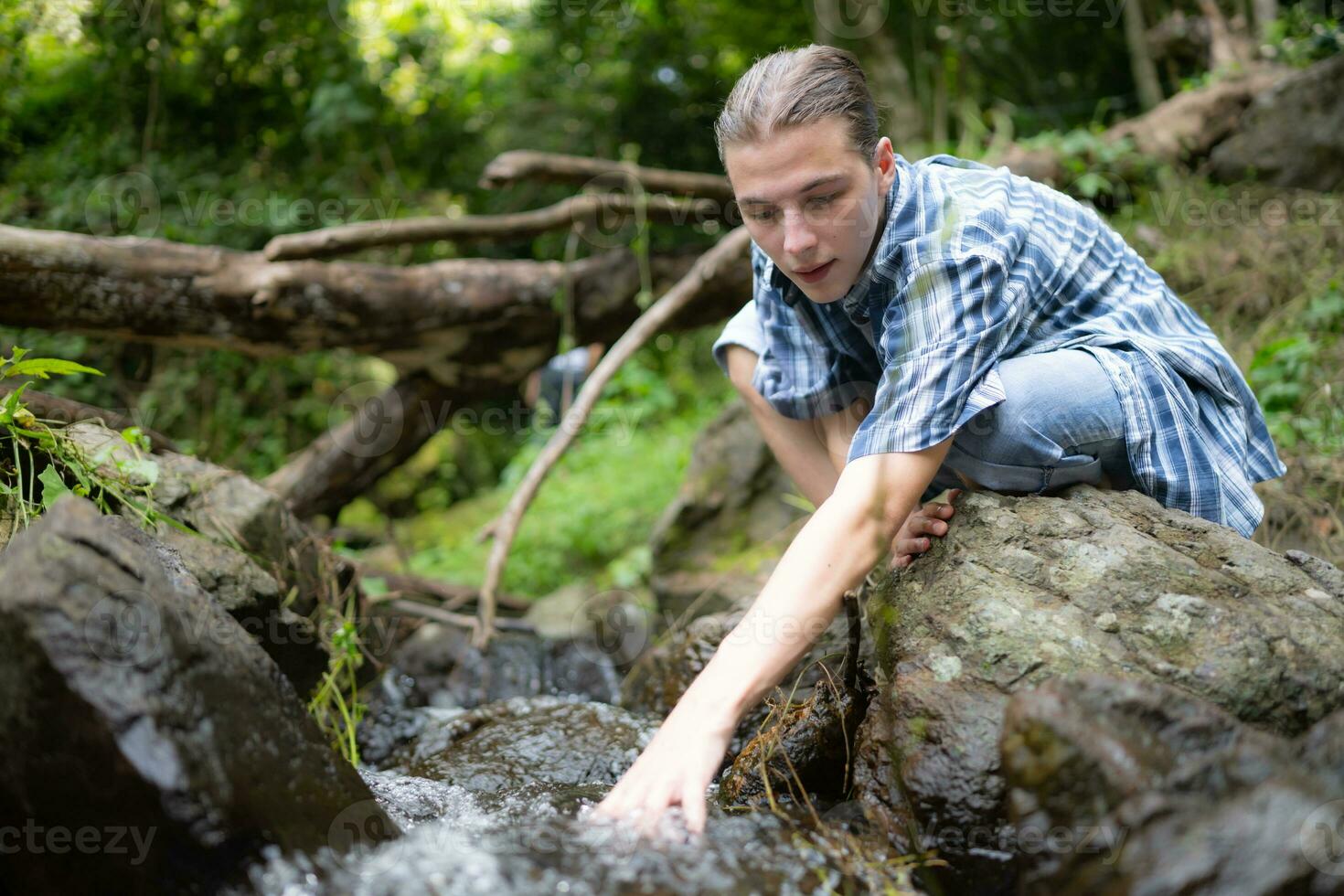 Hiker in the jungle playing with water in a stream in the forest. photo