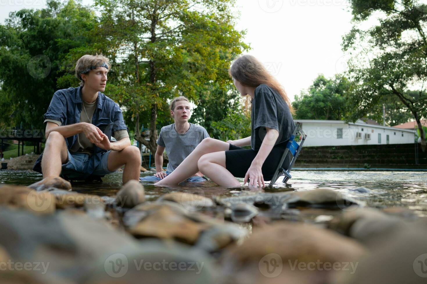 Group of friends are talking and having fun in the middle of the river flowing in front of the campsite. photo