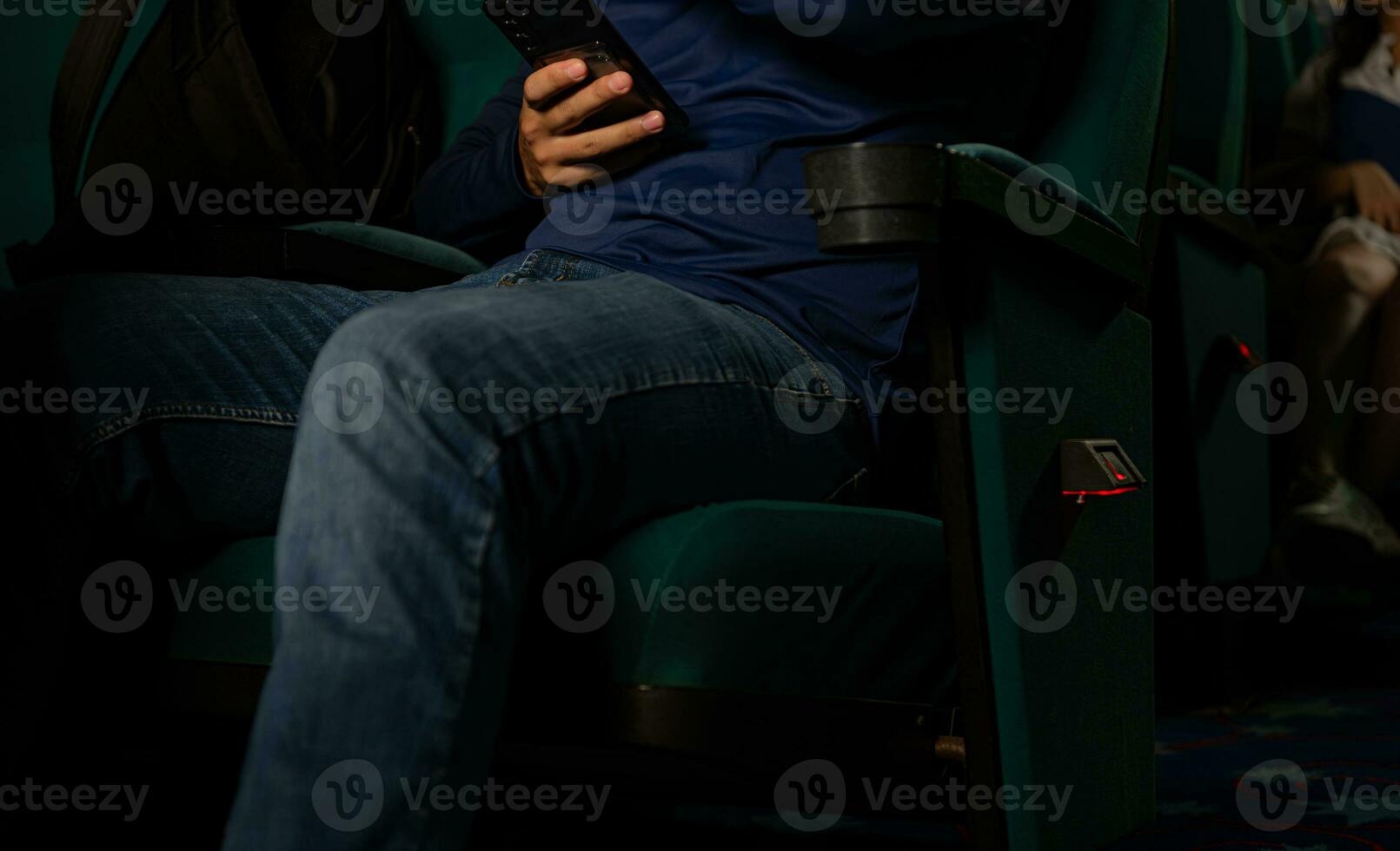 Young man sitting in a chair and using his mobile phone in the cinema photo