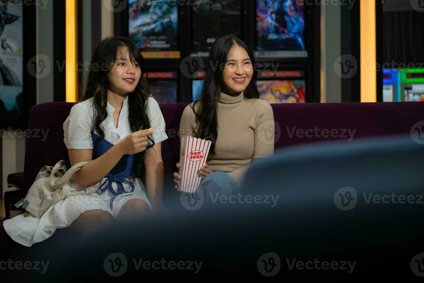 dos joven asiático mujer comiendo palomitas de maiz y esperando para acecho película a frente de cine foto
