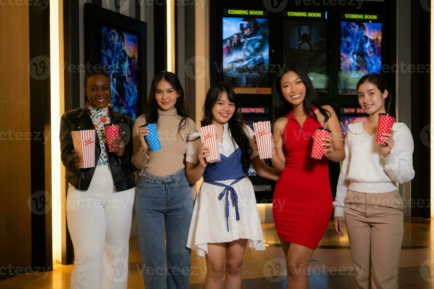Group of happy friends watching movie in cinema and eating popcorn at night photo
