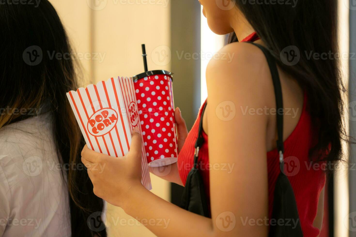 Young asian woman standing in line to buy movie tickets and in hand popcorn and drink photo