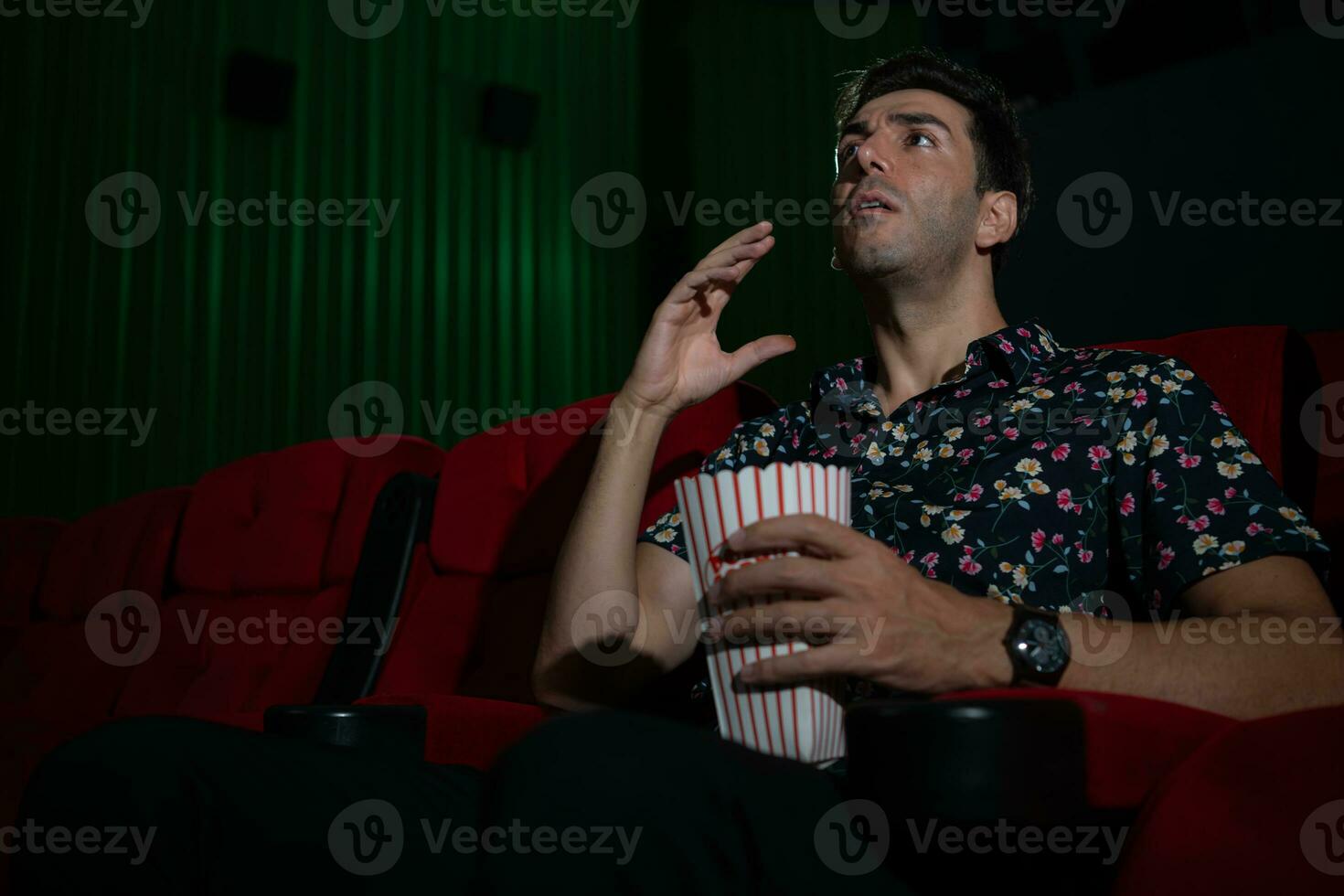 Young man watching movie and eating popcorn while sitting on red couch photo