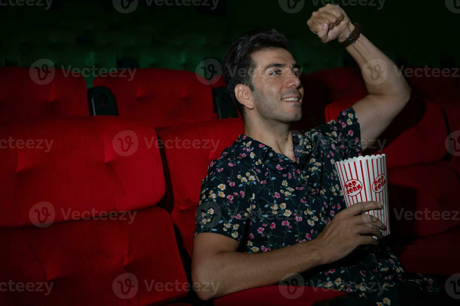 Young man watching movie and eating popcorn while sitting on red couch photo