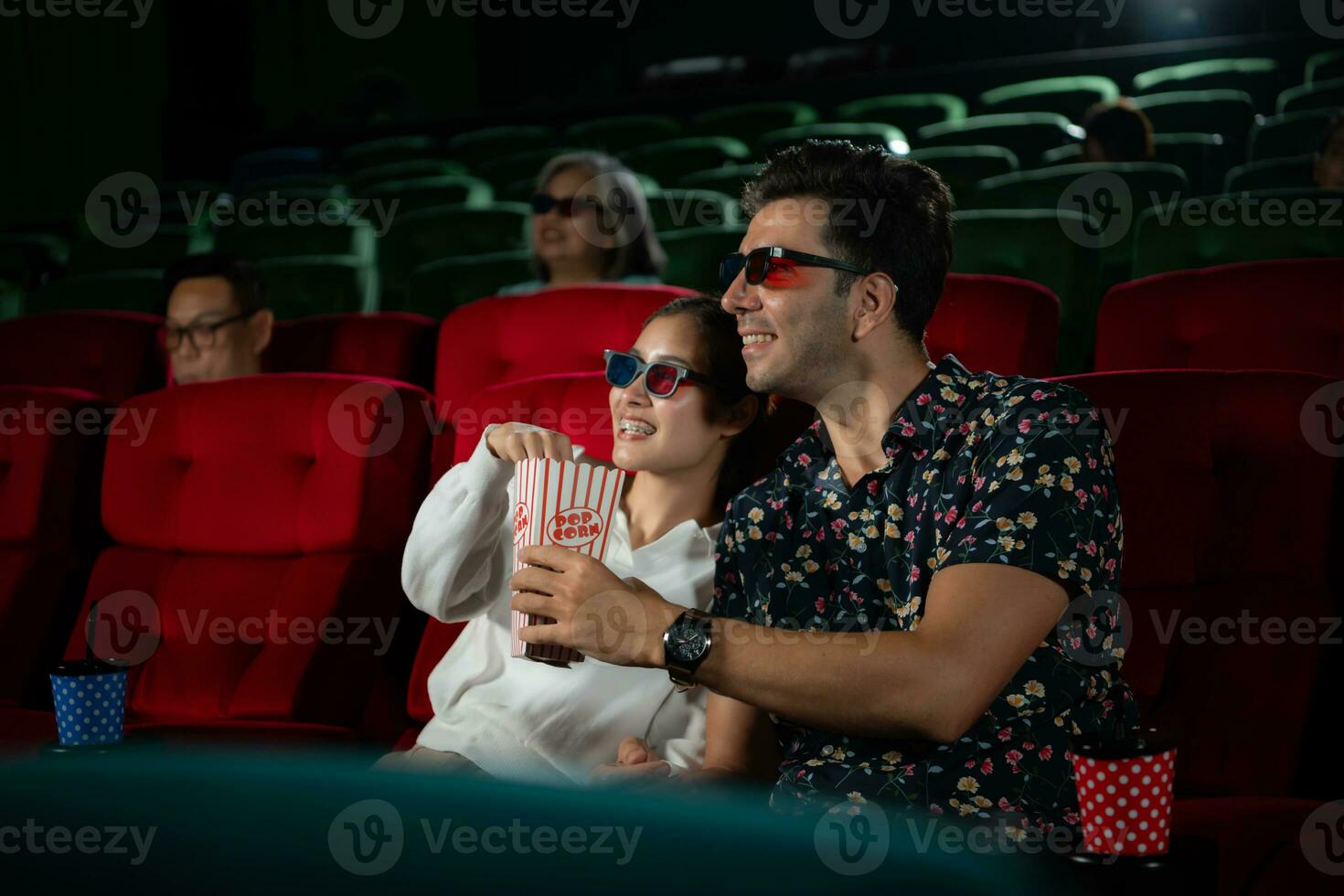 In a cinema, A young couple pair wearing 3D glasses watches movies and eats popcorn. photo