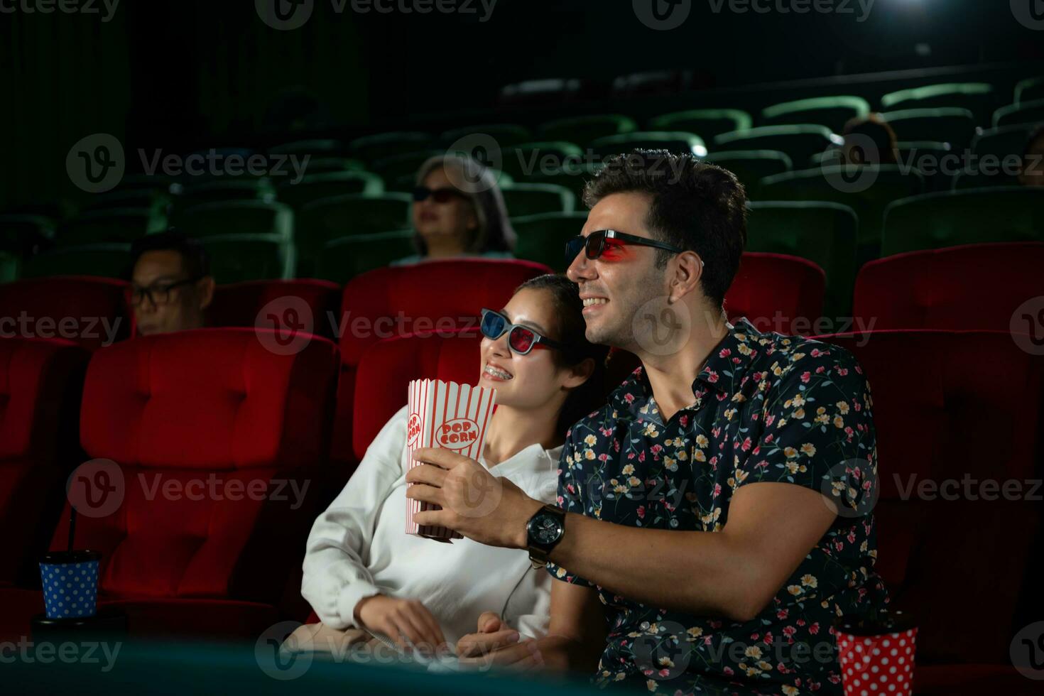 In a cinema, A young couple pair wearing 3D glasses watches movies and eats popcorn. photo