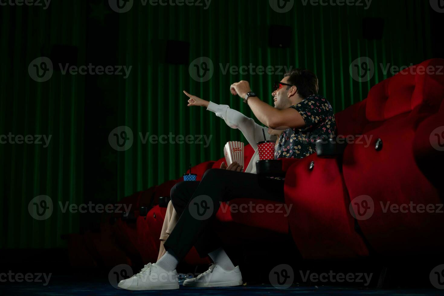 Young man and woman watching movie in cinema, sitting on red seats photo