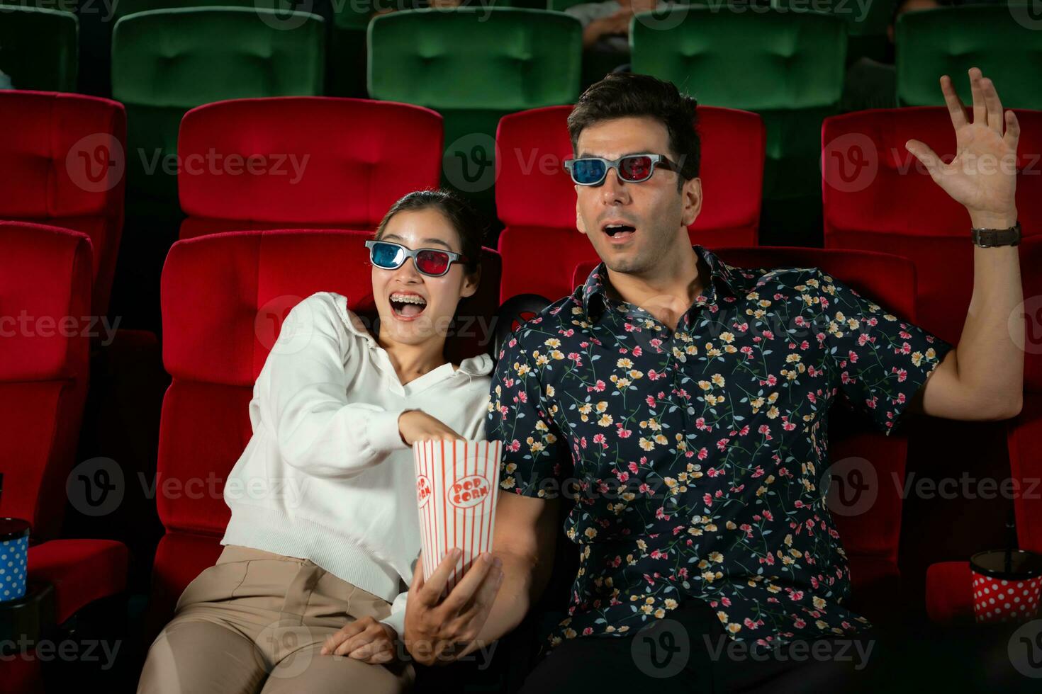 In a cinema, A young couple pair wearing 3D glasses watches movies and eats popcorn. photo