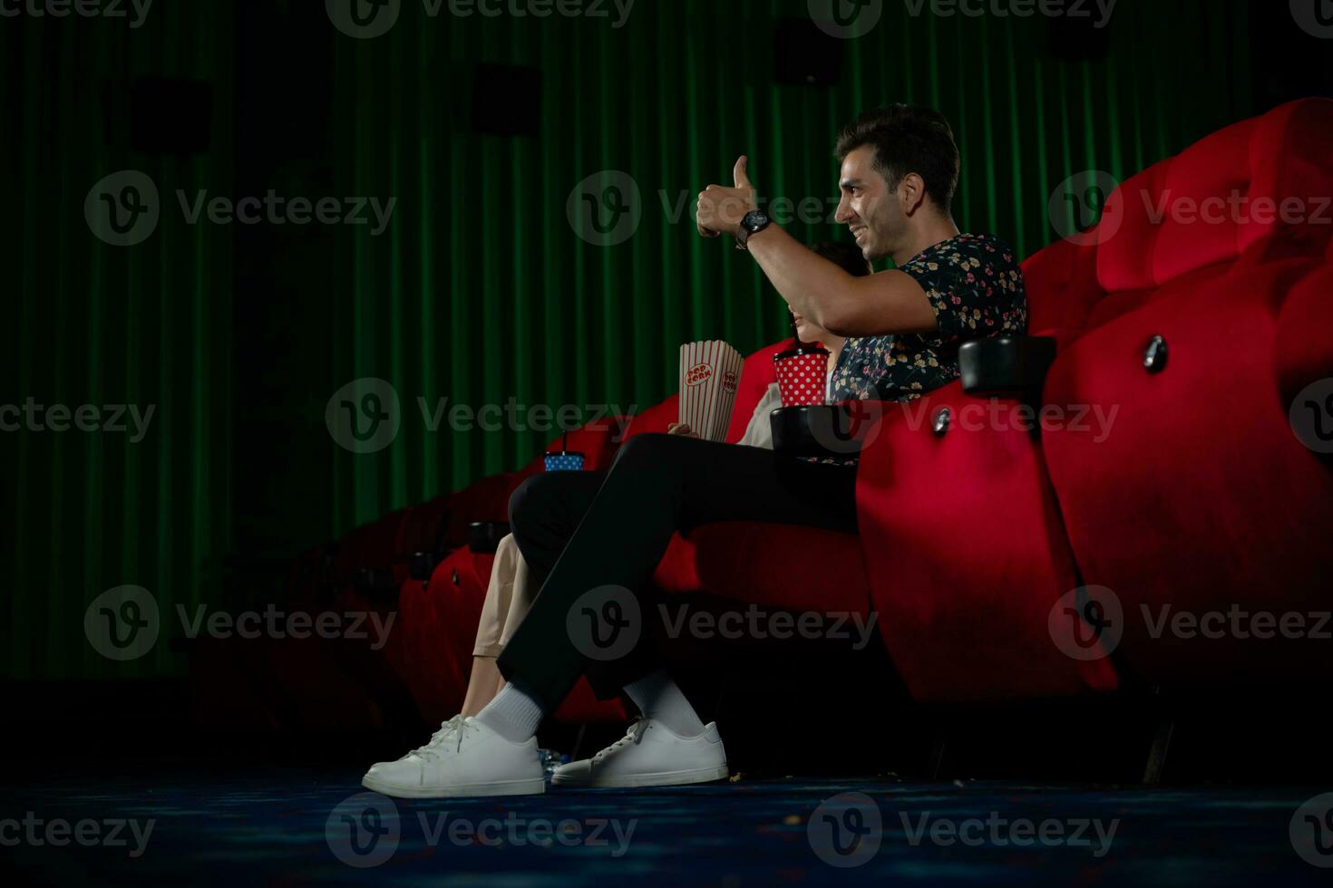 Young man and woman watching movie in cinema, sitting on red seats photo