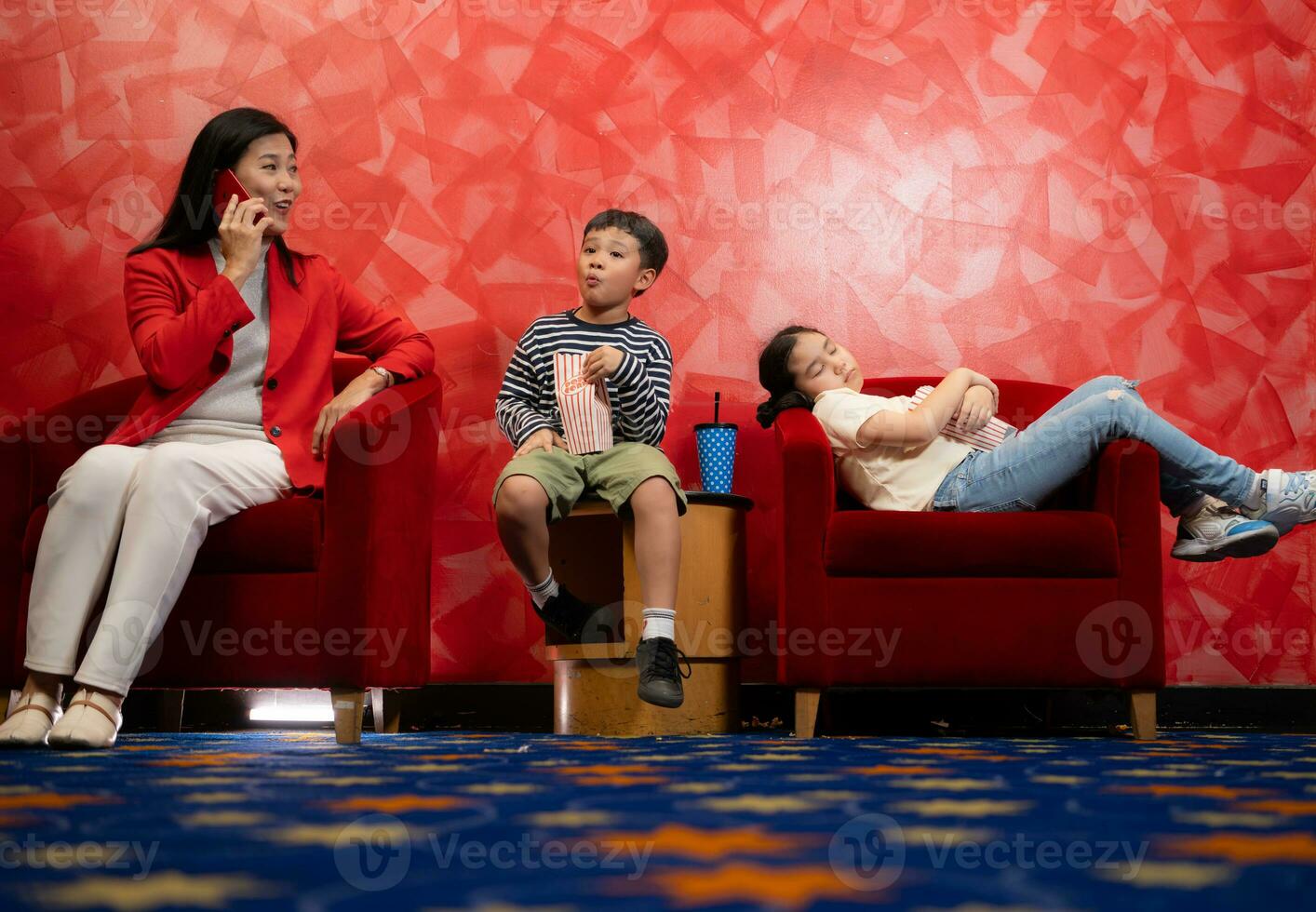 Mother and children watching movie in cinema, sitting on red armchair photo