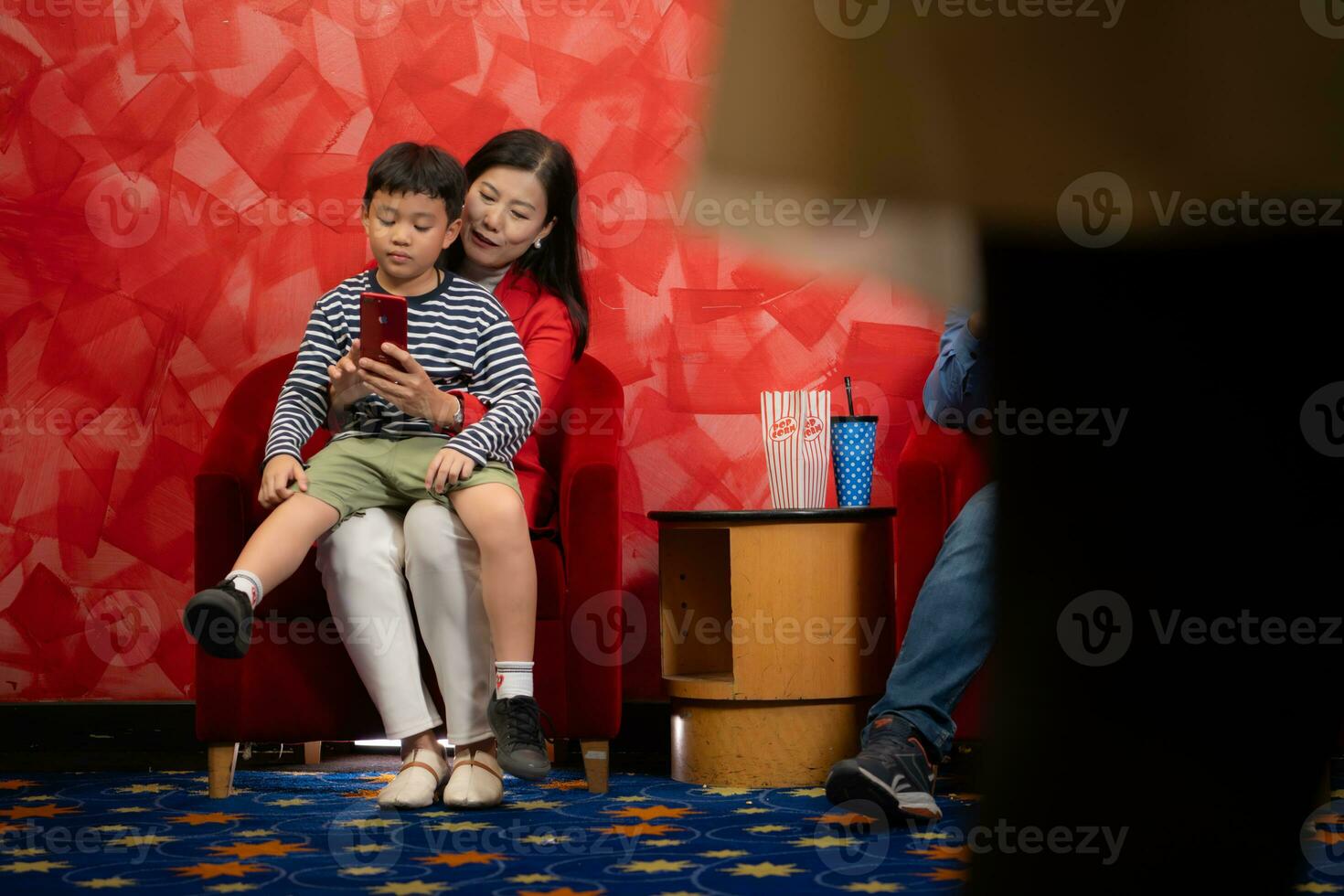 pequeño chico y su madre utilizando móvil teléfono mientras sentado en sofá en cine foto