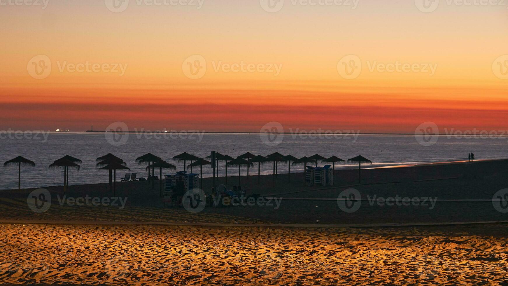 Golden Beach Twilight. Umbrella Silhouettes, Clouds, and Car Light on Sand photo