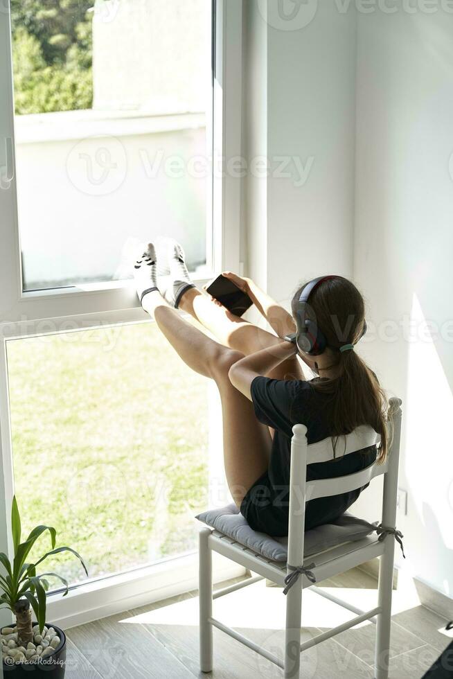 Young woman sitting in front of a well-lit window preparing to take a selfie with her smartphone photo