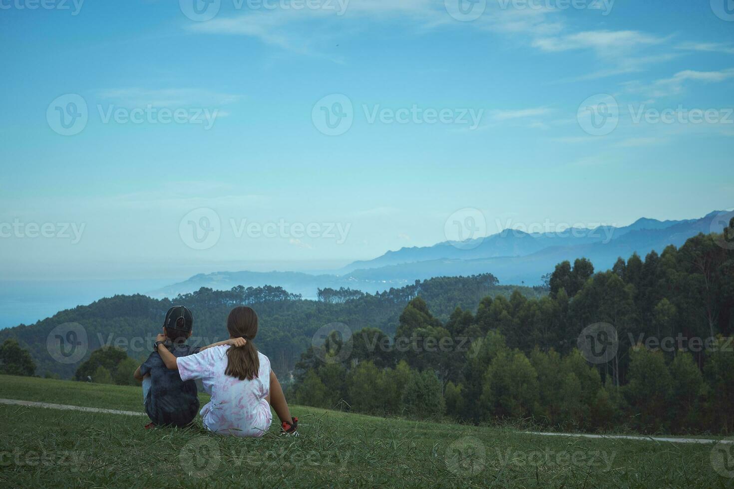 A couple of brothers hugging each other contemplate a beautiful green mountain landscape and coastal cliffs in the background photo