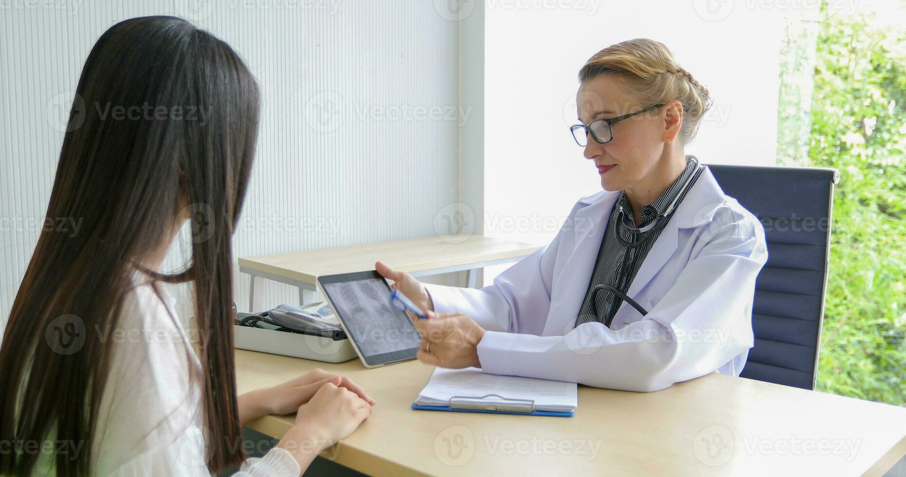 Asian woman patient sitting with doctor about her illness and showing x-ray results with blood pressure and heart rate measurement with stethoscope photo