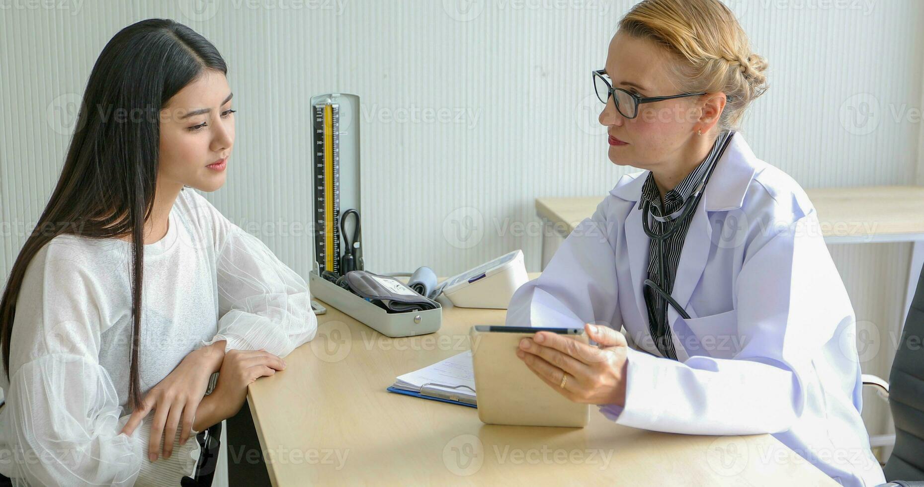 Asian woman patient sitting with doctor about her illness and showing x-ray results with blood pressure and heart rate measurement with stethoscope photo