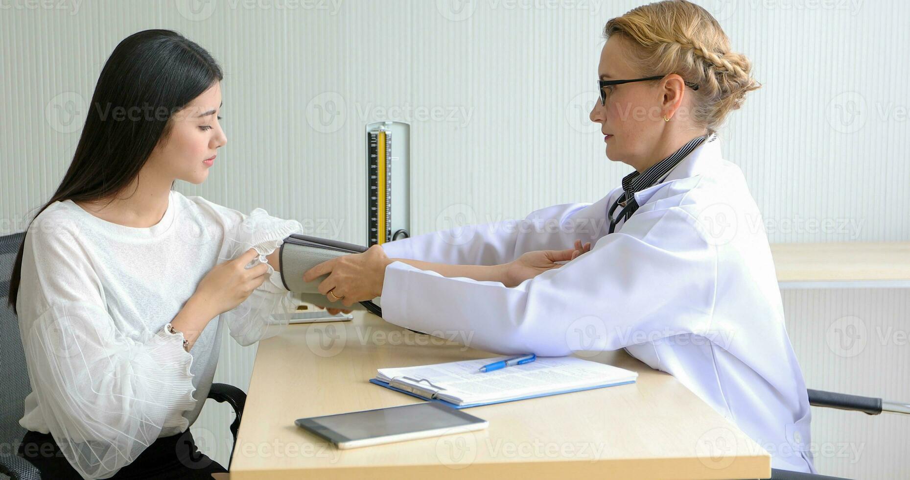 Asian woman patient sitting with doctor about her illness and showing x-ray results with blood pressure and heart rate measurement with stethoscope photo