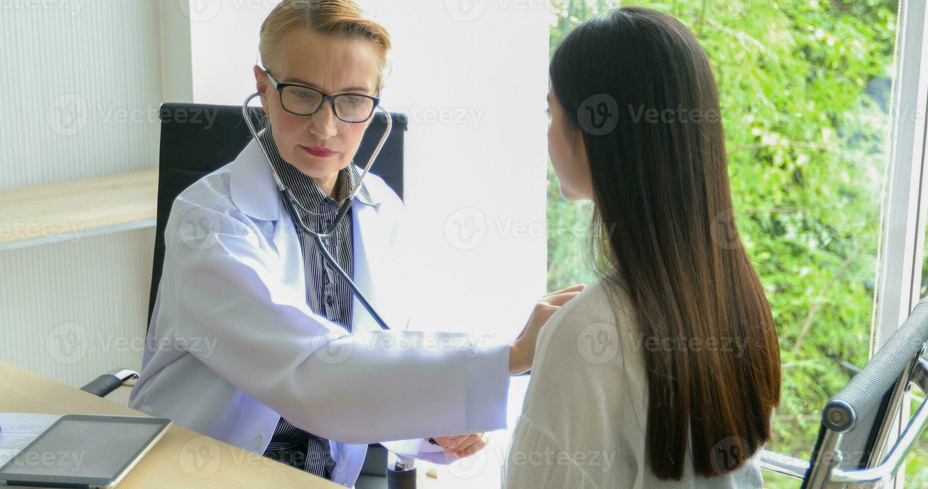 Asian woman patient sitting with doctor about her illness and showing x-ray results with blood pressure and heart rate measurement with stethoscope photo