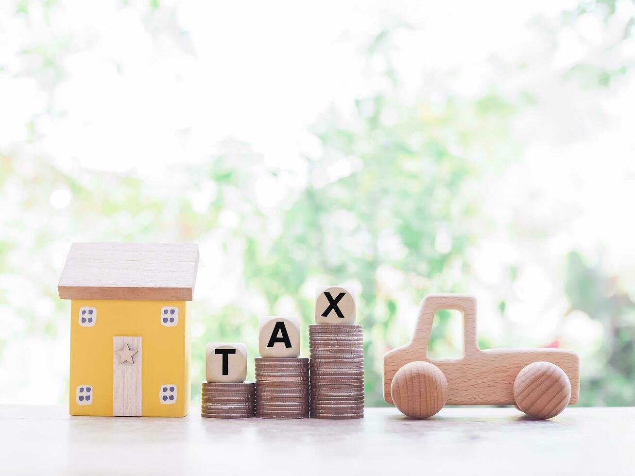 Wooden toy car, Miniature house and wooden blocks with the word TAX on stack of coins, The concept of paying tax for house or property and car photo