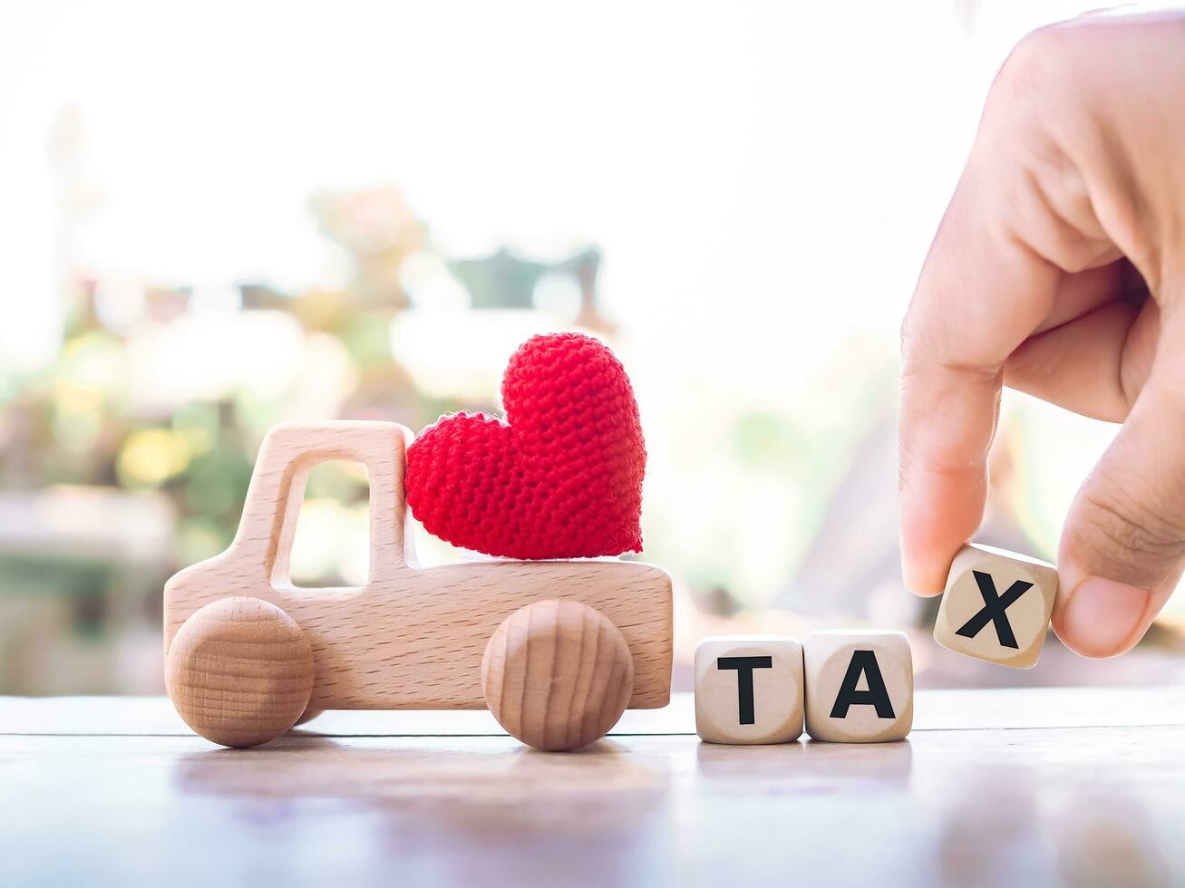 Close up hand holding wooden block with word TAX, wooden toy car with red heart. The concept of paying tax for car. Car taxes. photo