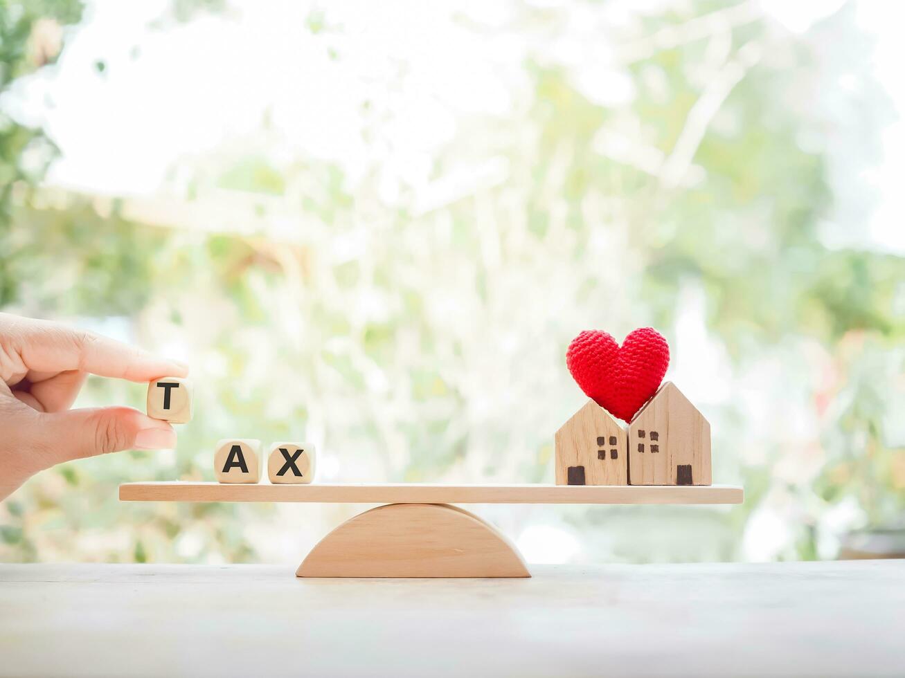 Close up hand holding wooden block with word TAX and miniature house on balancing scale. The concept of paying tax for house and property. photo