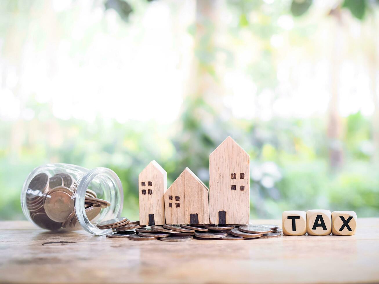 Miniature house on stack of coins and wooden blocks with the word TAX. The concept of paying tax for house and property. Property taxes. photo