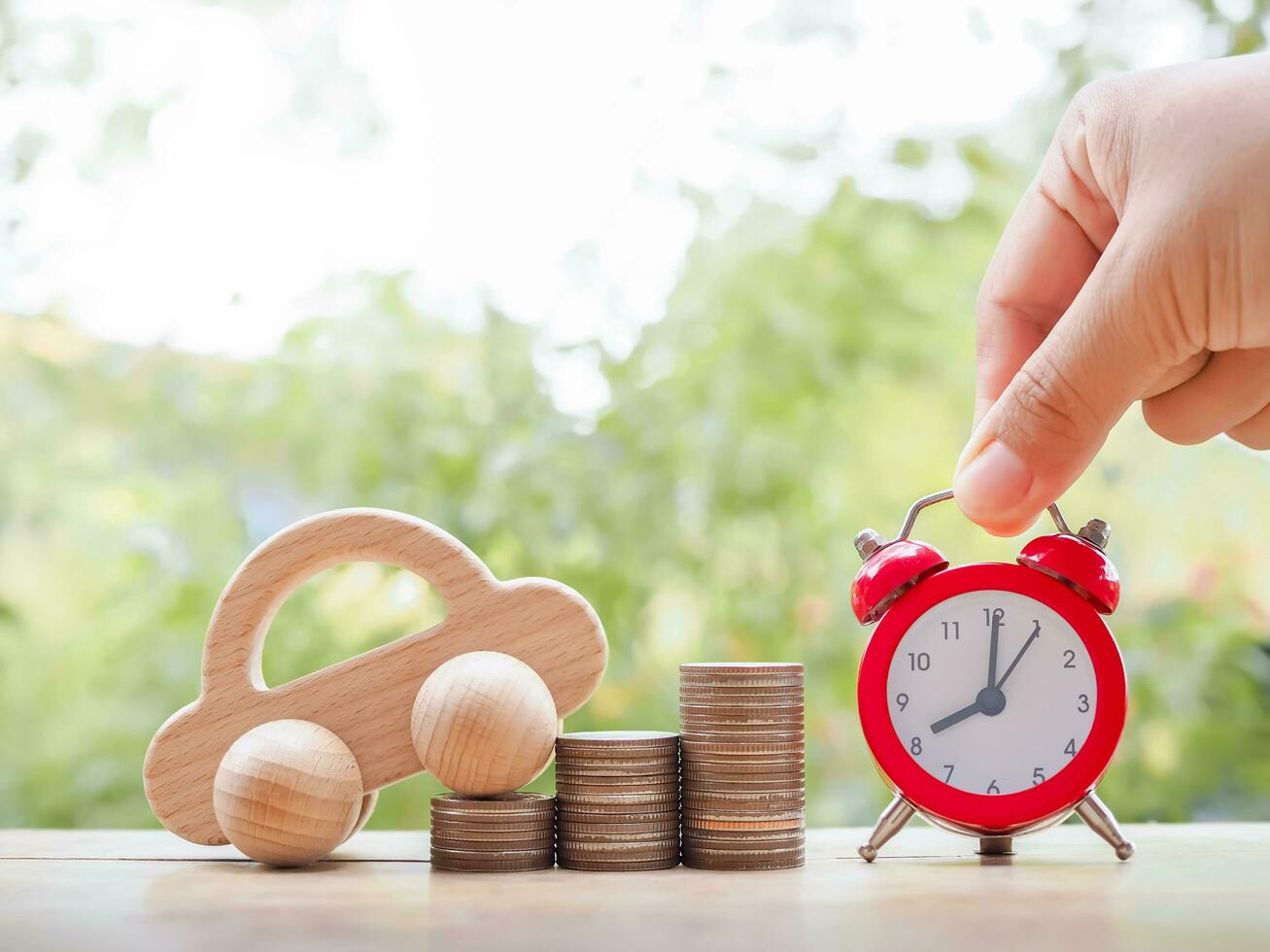 Close up hand arranging red alarm and wooden toy car on stack of coins. The concept of saving for car. photo