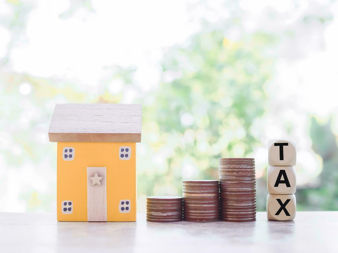 Miniature house, wooden blocks with the word TAX and stack of coins. The concept of paying tax for house and Property investment, House mortgage, Real estste. photo