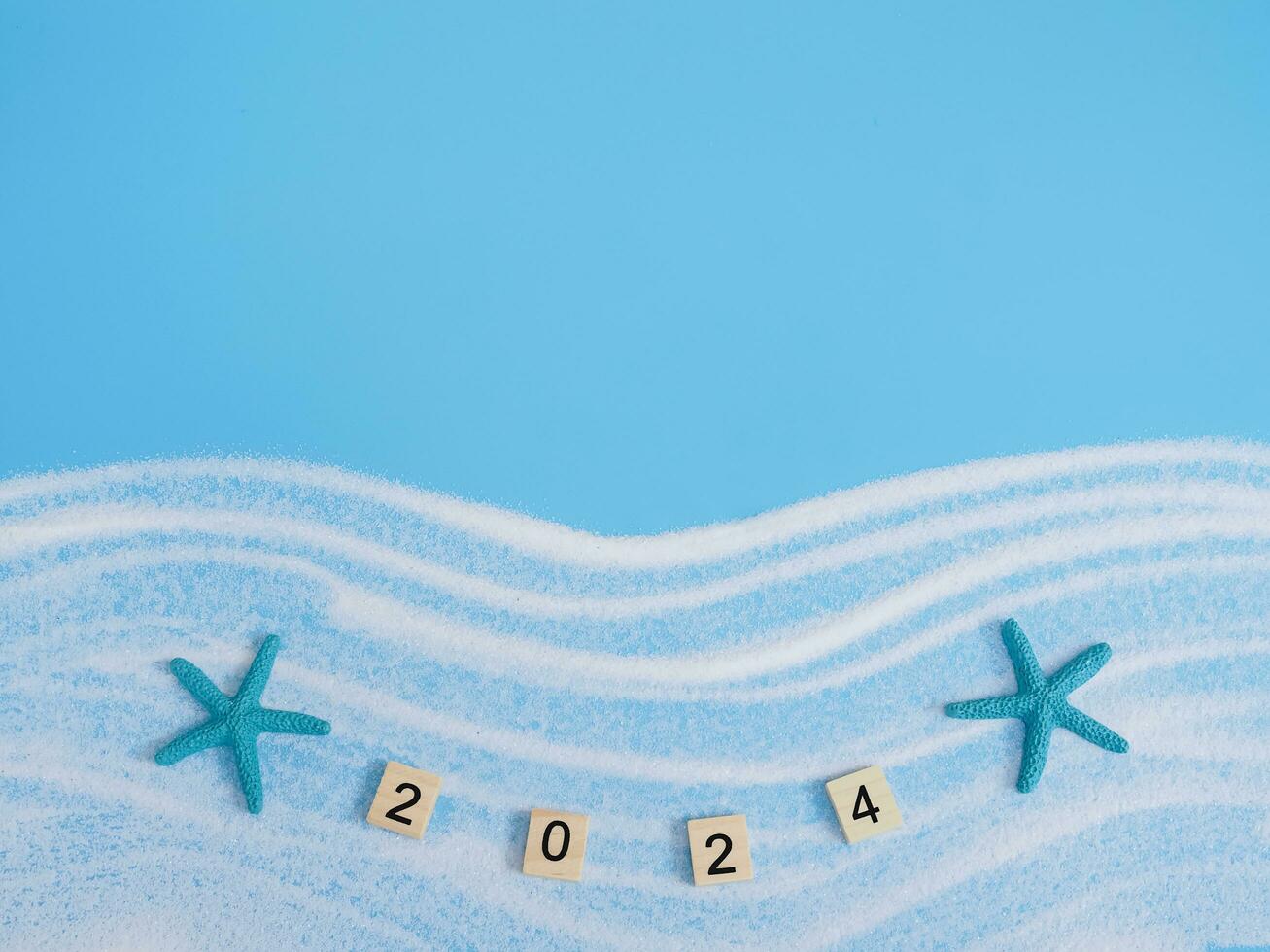 Wooden block with number 2024, seashells, starfish and white sand on blue background. Top view with copy space of summer background. The concept for summer of new year 2024 photo