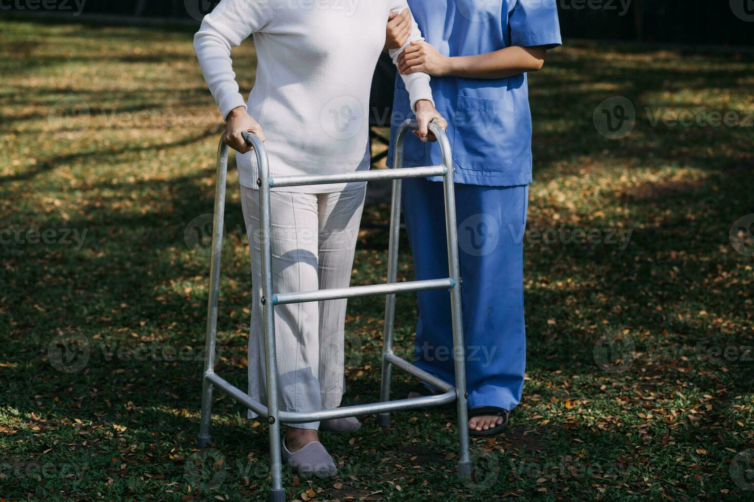 Asian young woman nurse at nursing home take care disabled senior man. Caregiver doctor serve physical therapy for older elderly patient to exercise and practice walking on walker or cane at backyard. photo