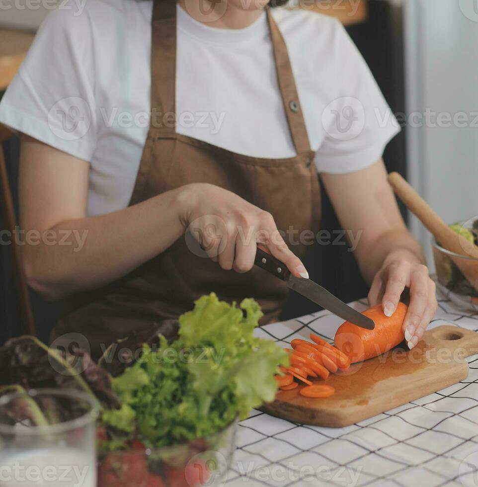 Delicious fruit and vegetables on a table and woman cooking. Housewife is cutting green cucumbers on a wooden board for making fresh salad in the kitchen. photo