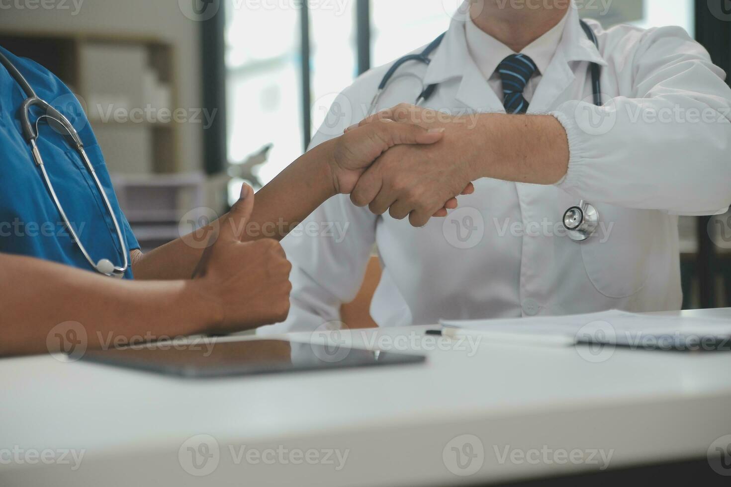 Doctor and patient shaking hands in the office, they are sitting at desk, hands close up photo