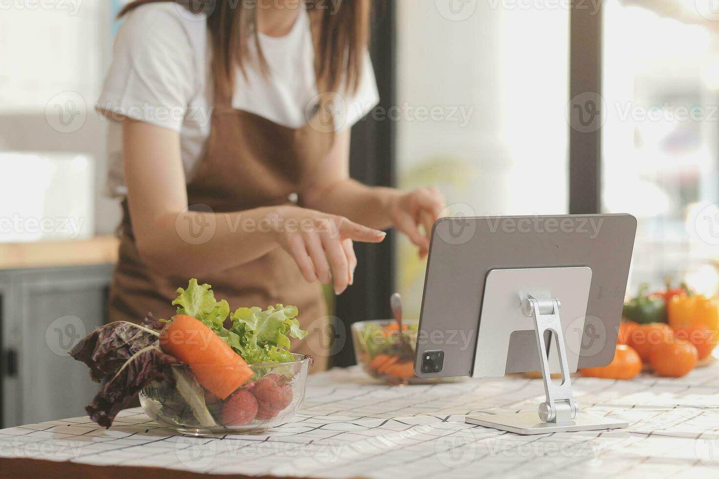 Delicious fruit and vegetables on a table and woman cooking. Housewife is cutting green cucumbers on a wooden board for making fresh salad in the kitchen. photo