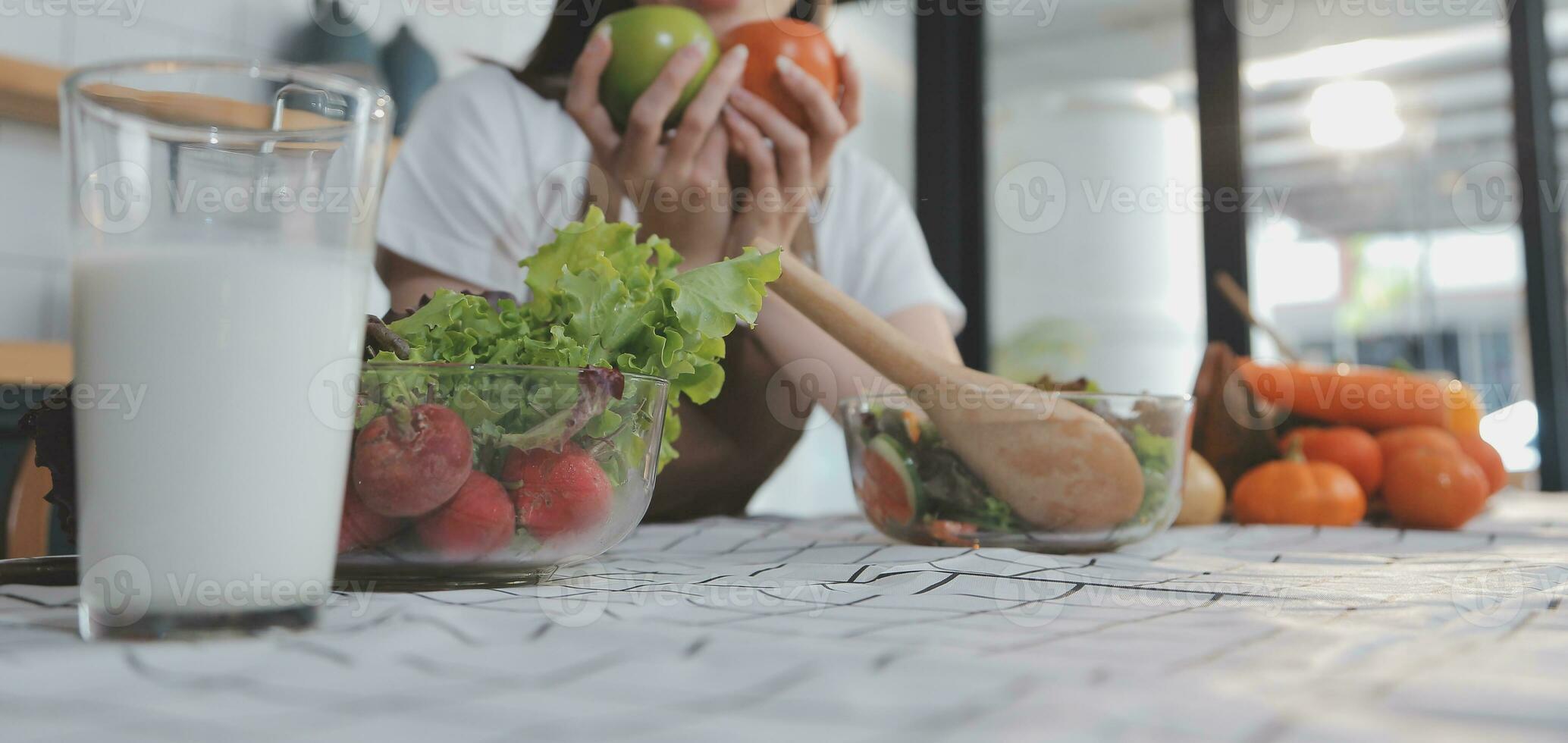 Delicious fruit and vegetables on a table and woman cooking. Housewife is cutting green cucumbers on a wooden board for making fresh salad in the kitchen. photo