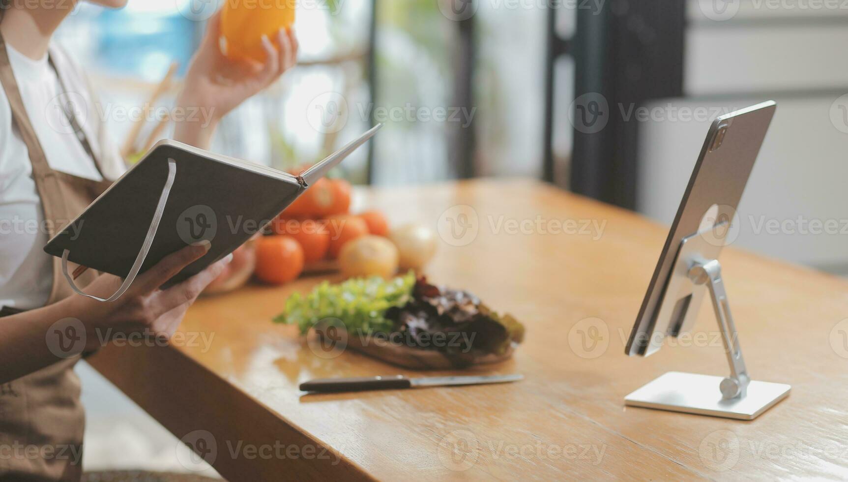 Delicious fruit and vegetables on a table and woman cooking. Housewife is cutting green cucumbers on a wooden board for making fresh salad in the kitchen. photo
