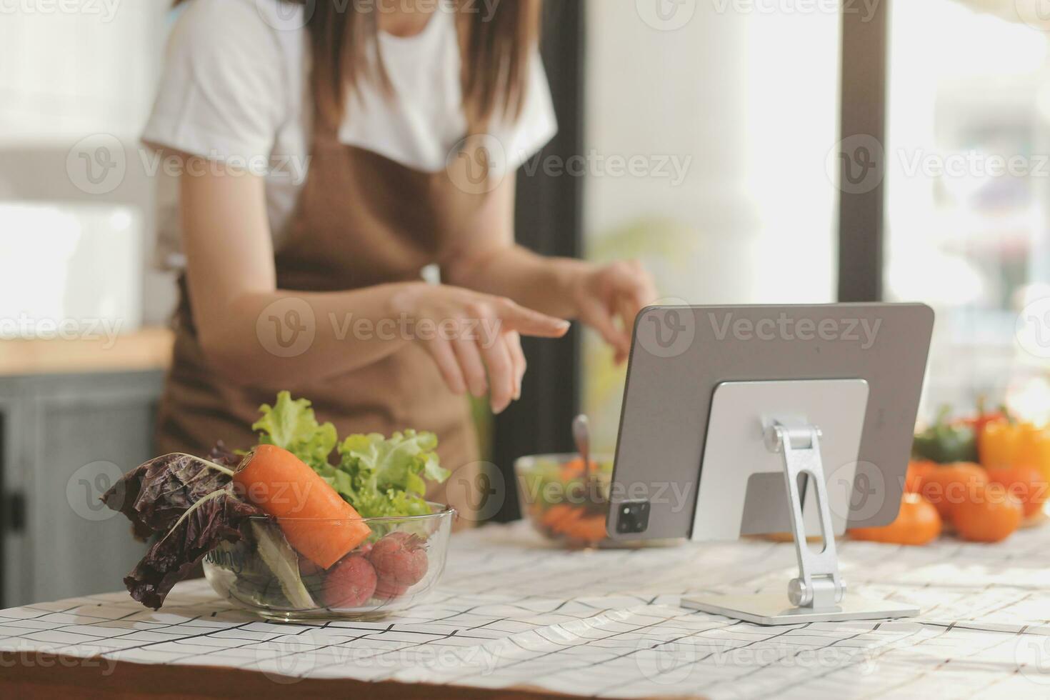 Delicious fruit and vegetables on a table and woman cooking. Housewife is cutting green cucumbers on a wooden board for making fresh salad in the kitchen. photo