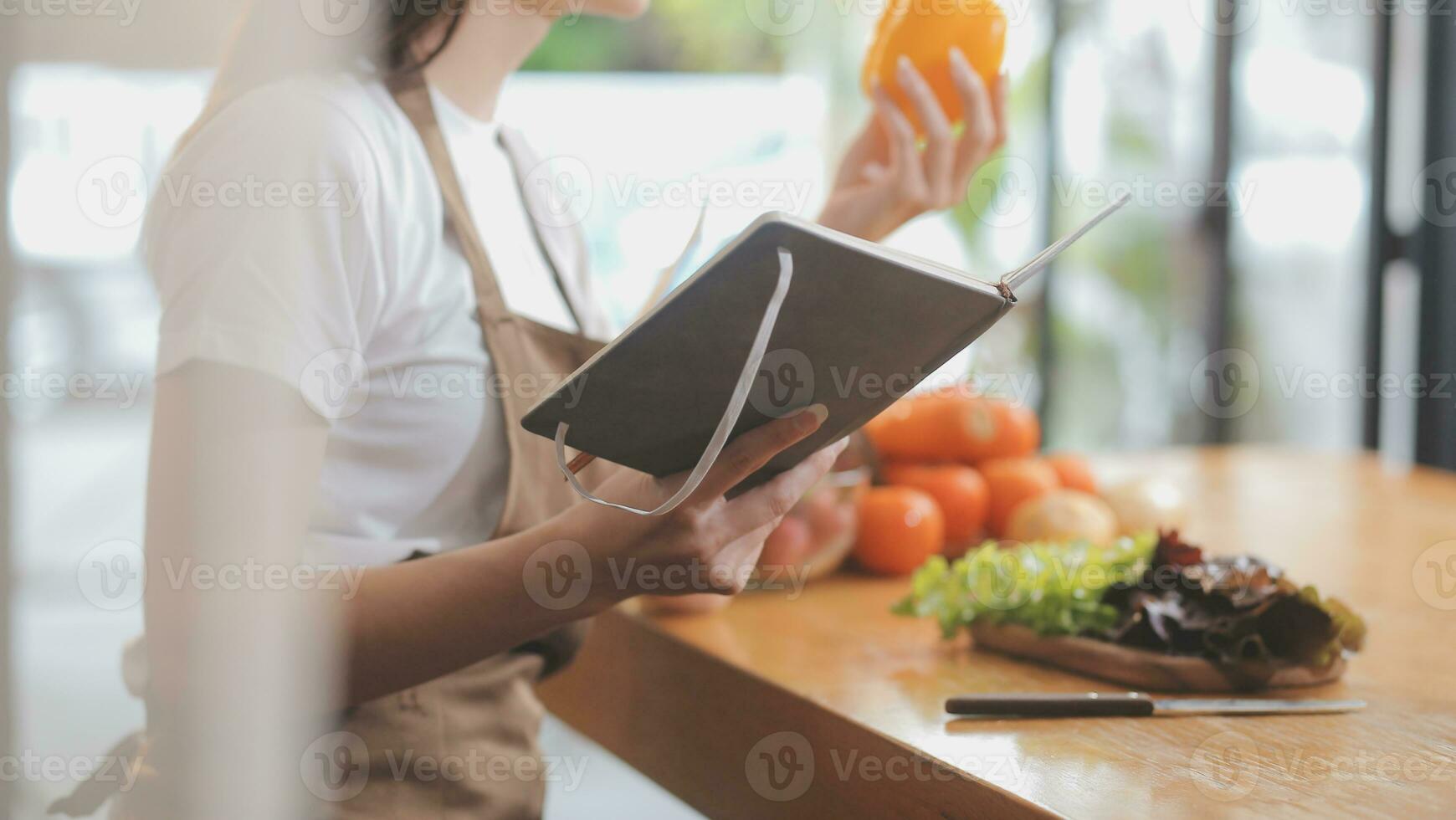 Delicious fruit and vegetables on a table and woman cooking. Housewife is cutting green cucumbers on a wooden board for making fresh salad in the kitchen. photo
