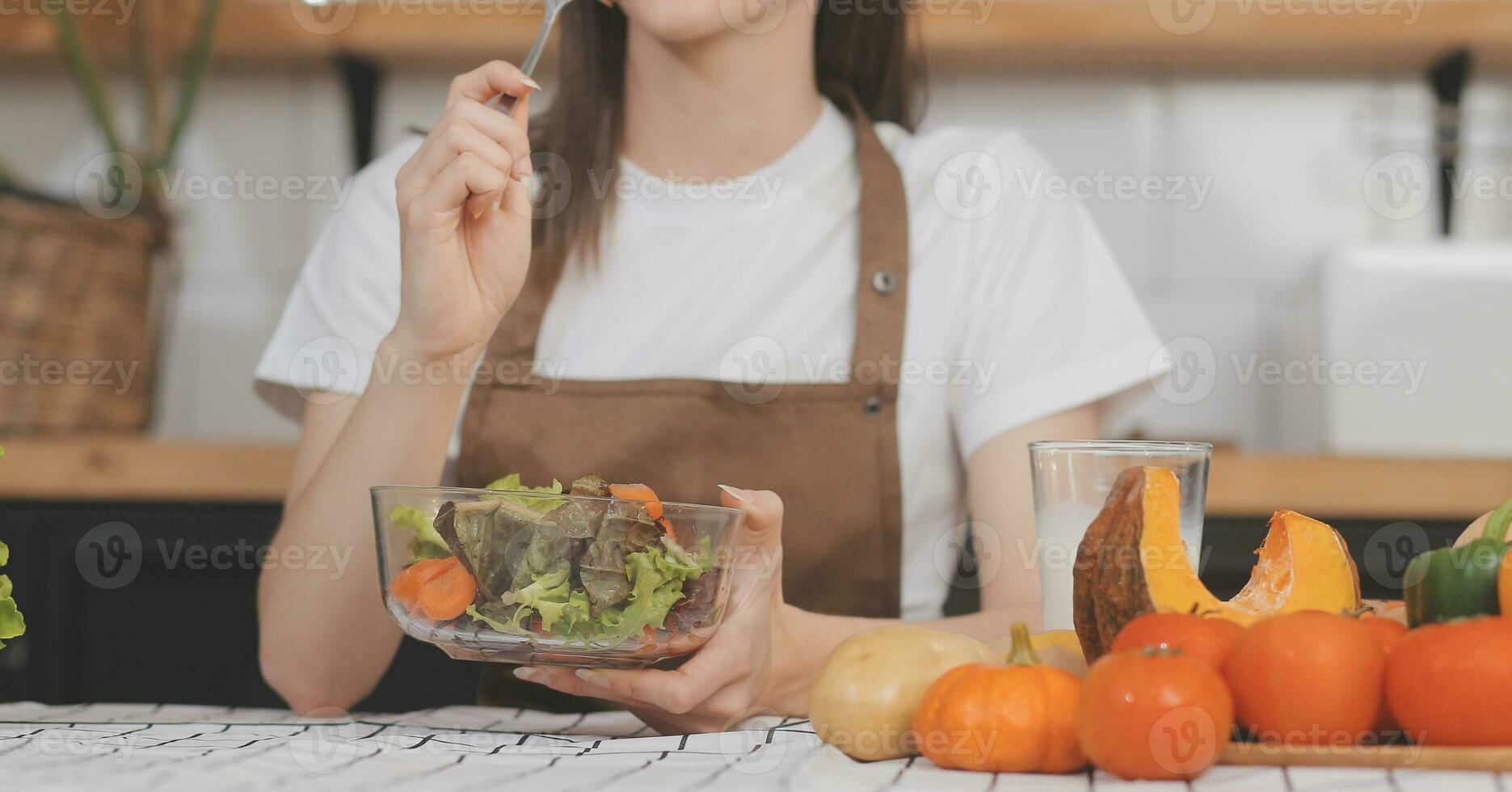 Delicious fruit and vegetables on a table and woman cooking. Housewife is cutting green cucumbers on a wooden board for making fresh salad in the kitchen. photo