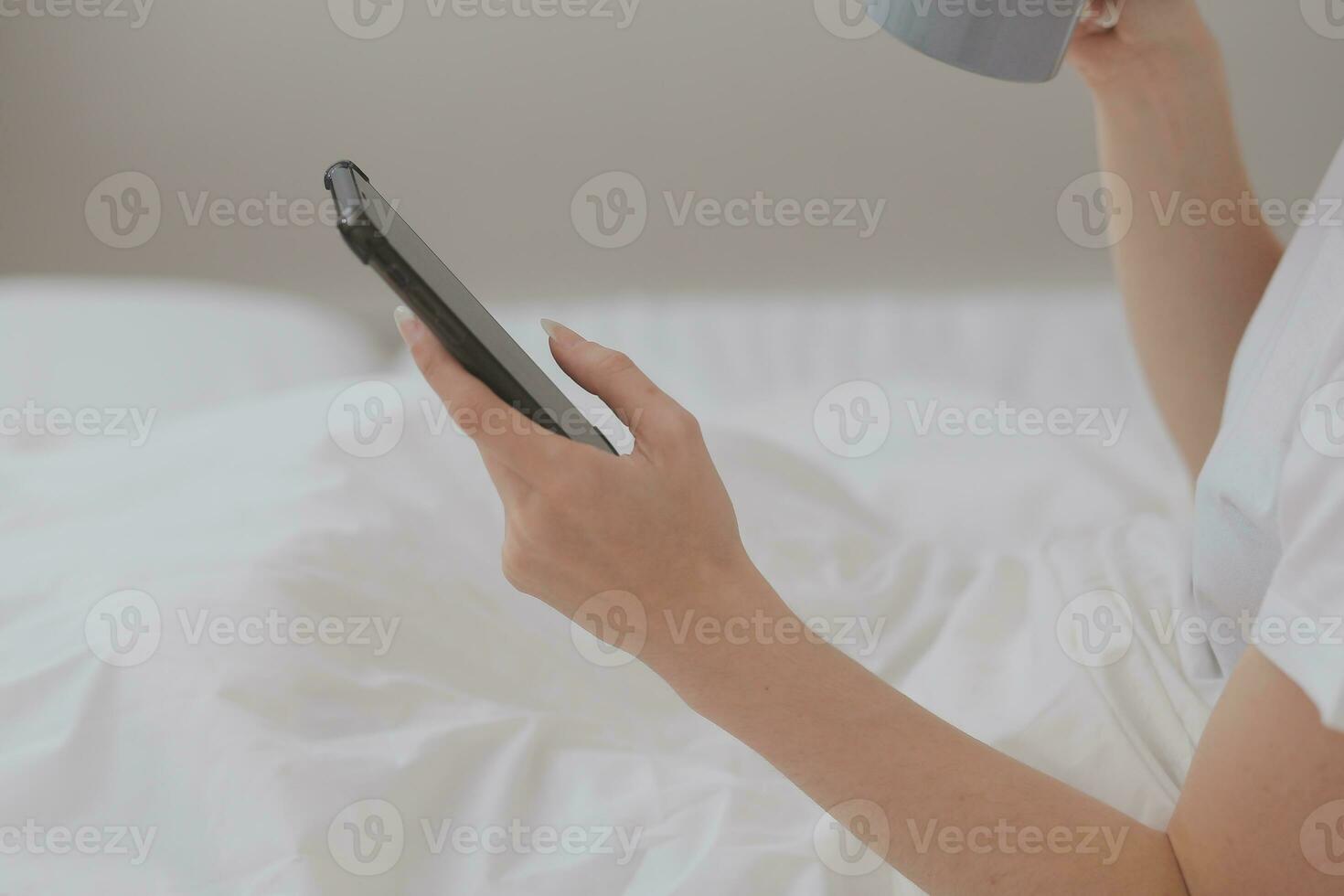 Efficient Young Millennial Girl Sitting on a Bed in the Morning, Uses Laptop Computer and Eats Croissants and Drinks Coffee for Breakfast photo