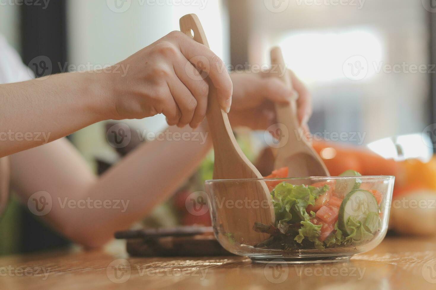Delicious fruit and vegetables on a table and woman cooking. Housewife is cutting green cucumbers on a wooden board for making fresh salad in the kitchen. photo