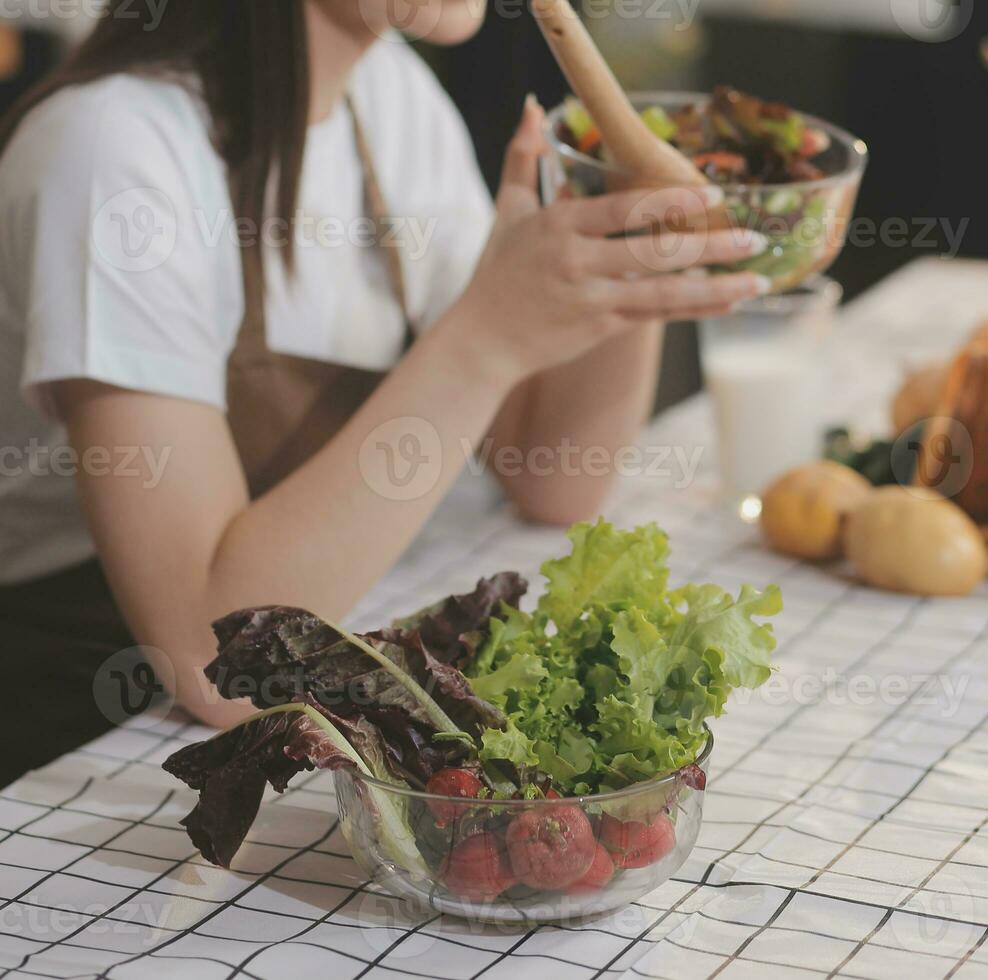 Delicious fruit and vegetables on a table and woman cooking. Housewife is cutting green cucumbers on a wooden board for making fresh salad in the kitchen. photo