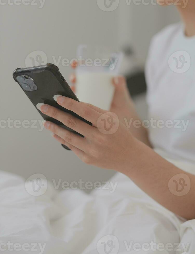 eficiente joven milenario niña sentado en un cama en el mañana, usos ordenador portátil computadora y come croissants y bebidas café para desayuno foto