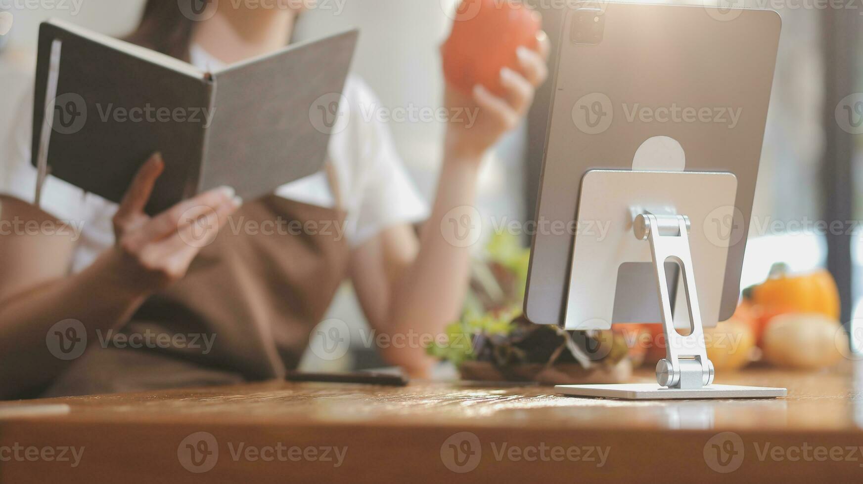 Delicious fruit and vegetables on a table and woman cooking. Housewife is cutting green cucumbers on a wooden board for making fresh salad in the kitchen. photo