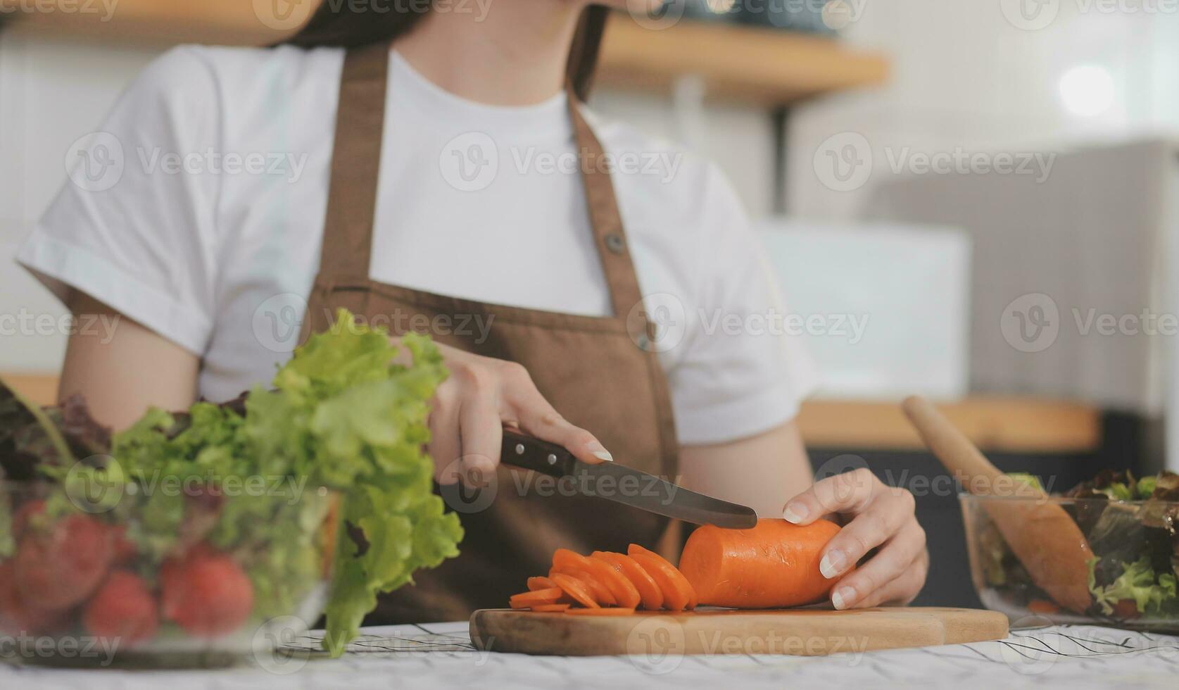 Delicious fruit and vegetables on a table and woman cooking. Housewife is cutting green cucumbers on a wooden board for making fresh salad in the kitchen. photo