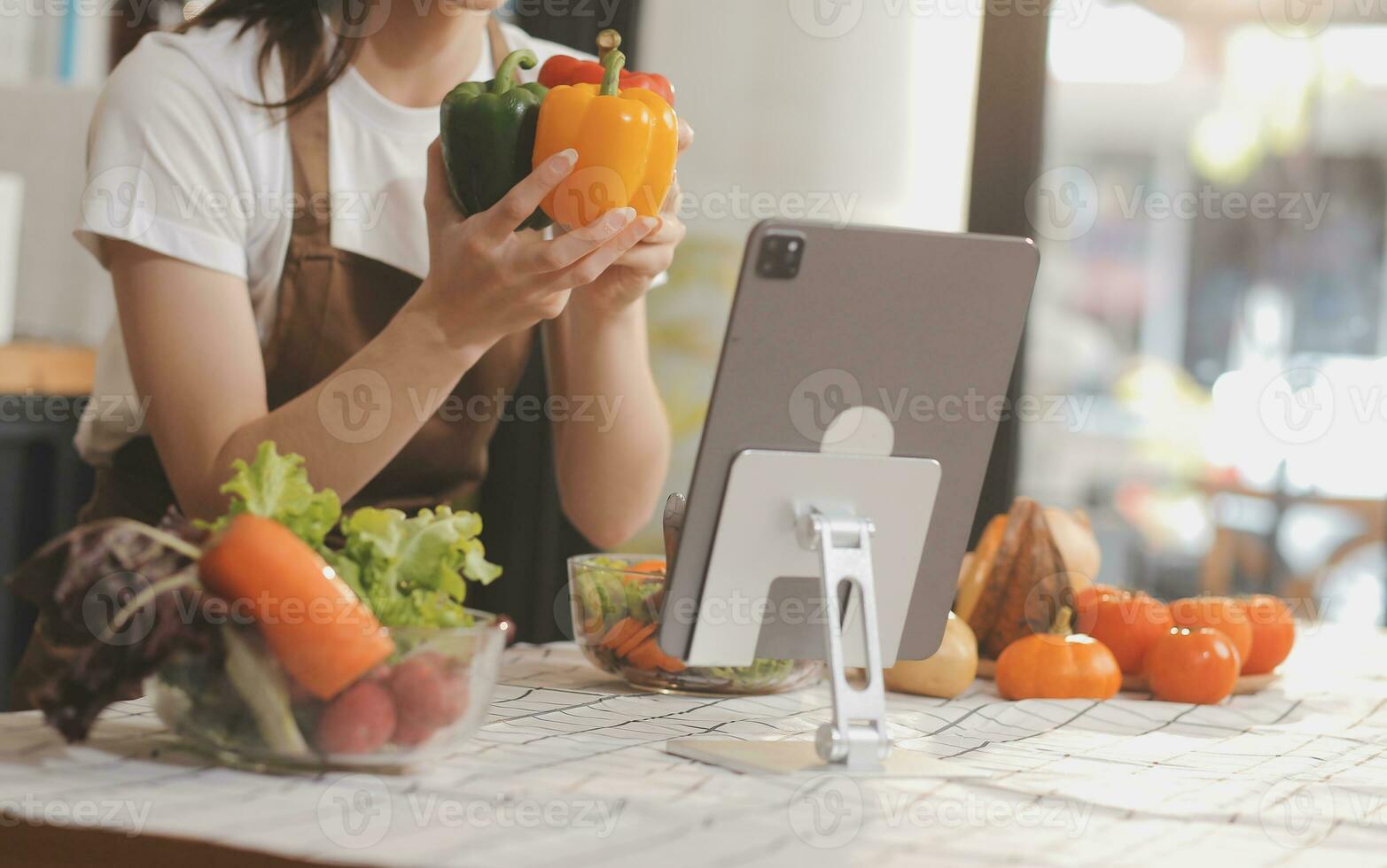 Delicious fruit and vegetables on a table and woman cooking. Housewife is cutting green cucumbers on a wooden board for making fresh salad in the kitchen. photo