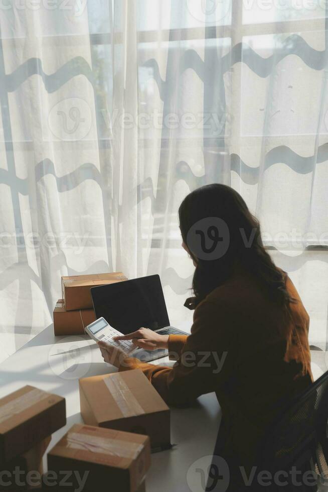 Portrait young attractive hipster asia female owner startup look at camera work happy with box at home prepare parcel delivery in sme supply chain, procurement, omnichannel ecommerce online concept. photo