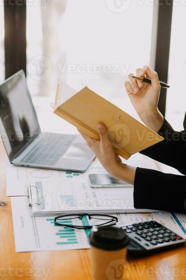 Asian Businesswoman Using laptop computer and working at office with calculator document on desk, doing planning analyzing the financial report, business plan investment, finance analysis concept. photo