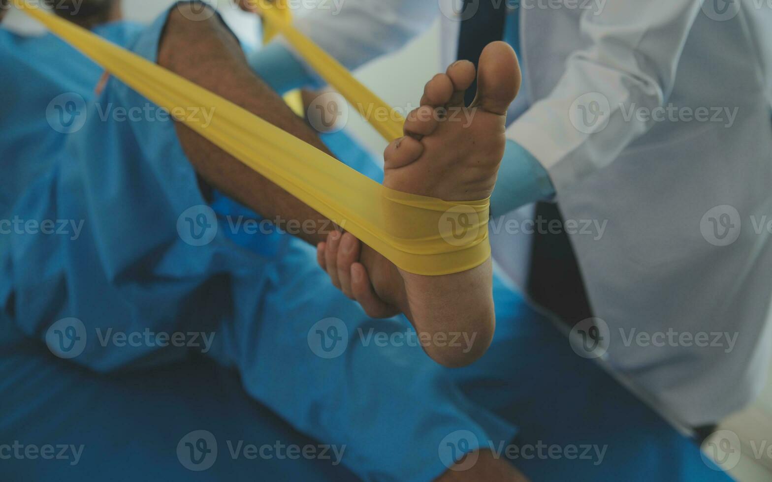 Male patient using elastic band while doing physical exercises for leg muscles at modern clinic, rehabilitation center or hospital. Close up of man's foot. Physiotherapy concept photo