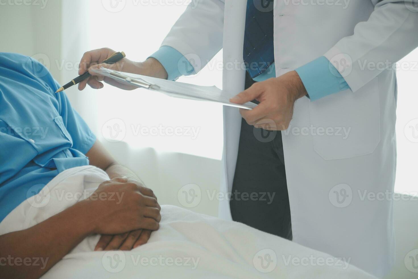 Close up of doctor sitting on bedside of male patient in hospital photo